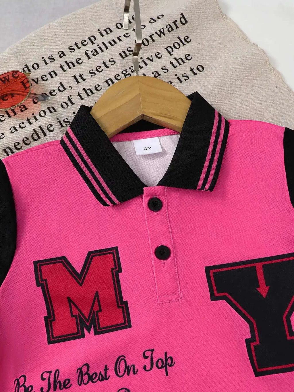 Kids rose pink polo shirt front with black collar stripes and large letter graphic