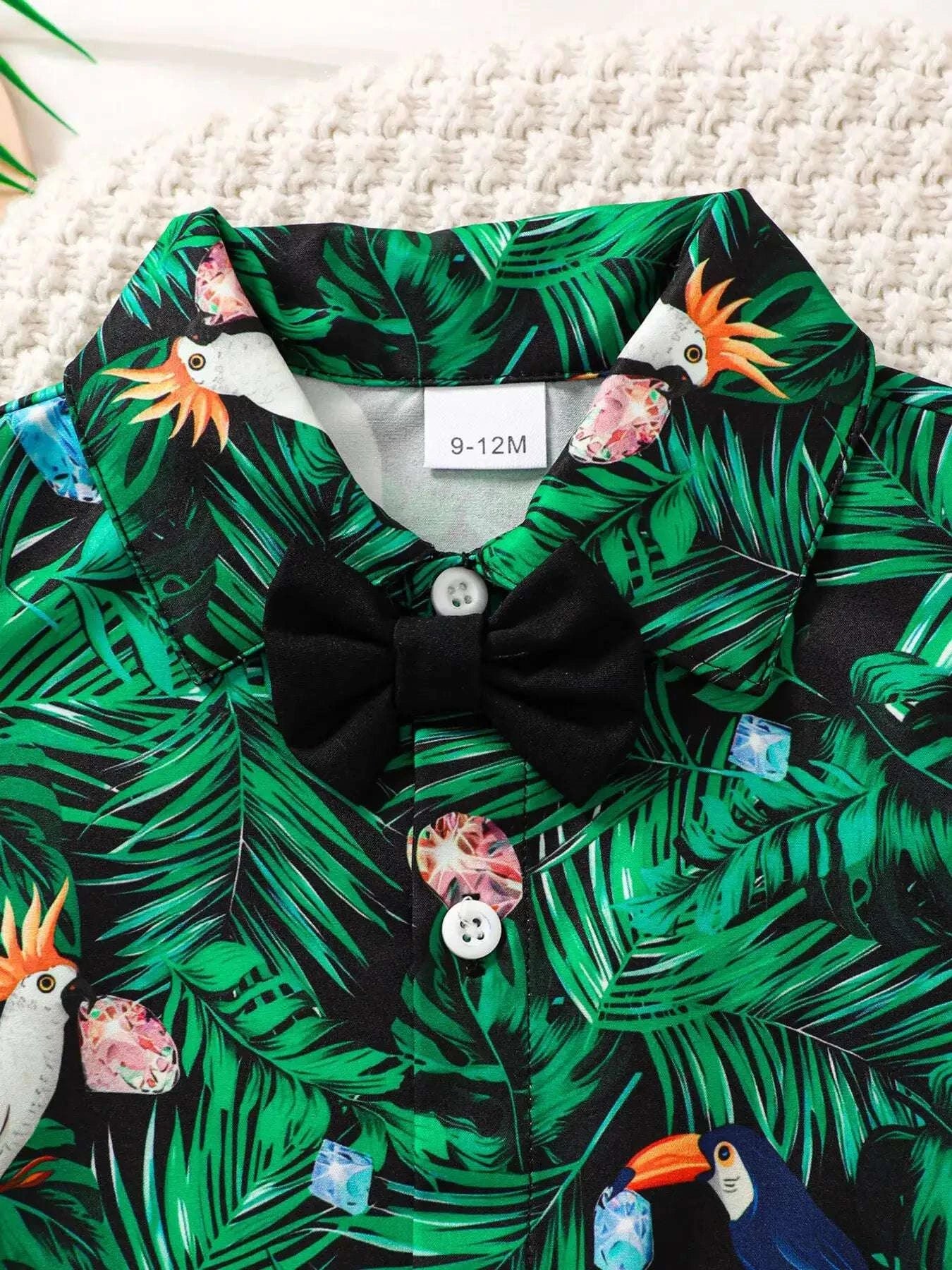 Green tropical print shirt close-up with black bow tie and white buttons.