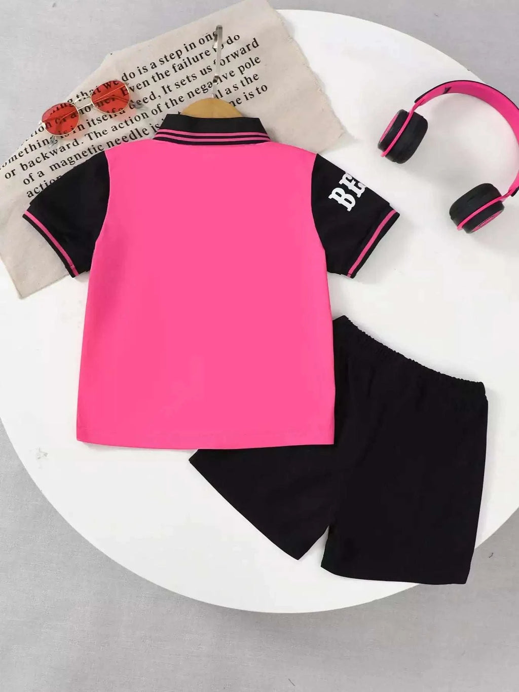 Kids rose pink polo shirt back view with black sleeve stripes; black shorts