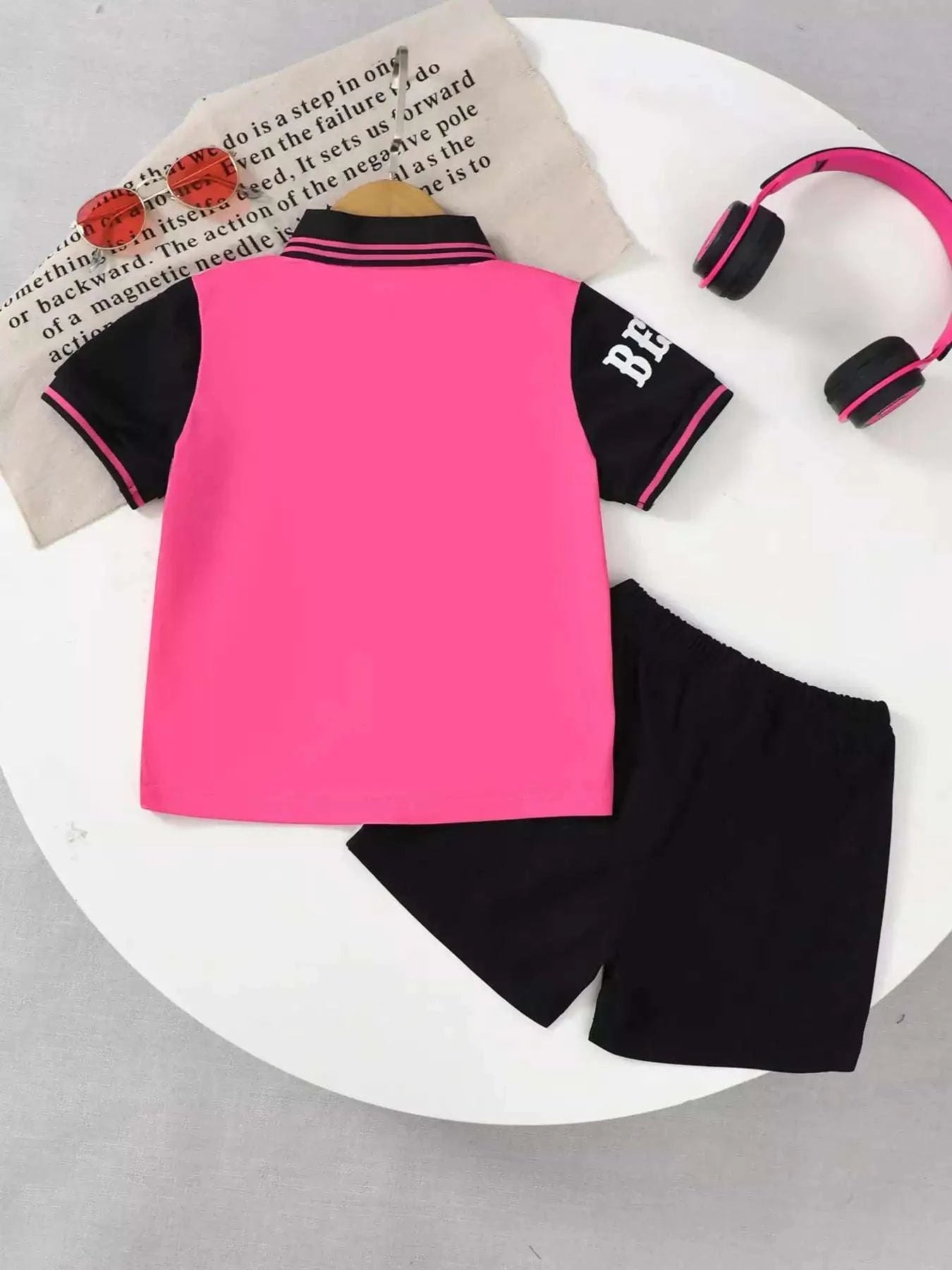 Kids rose pink polo shirt back view with black sleeve stripes; black shorts