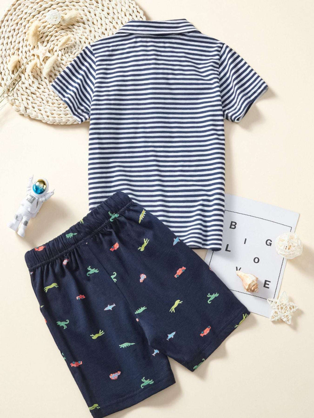 Children's striped polo shirt and dinosaur-print shorts set laid flat, navy and white