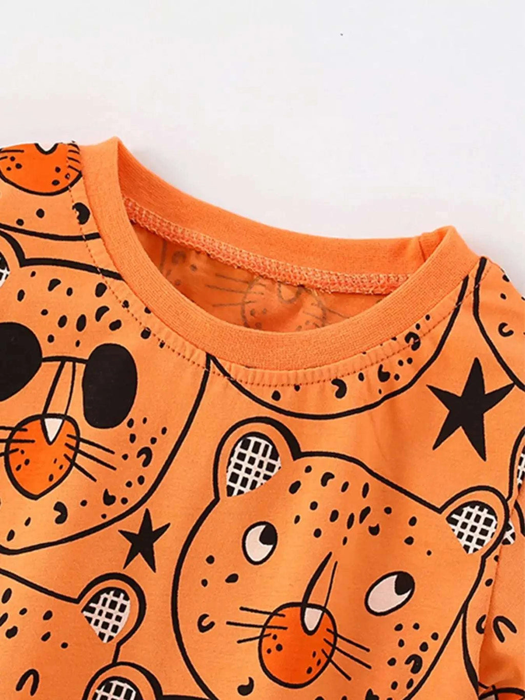 Orange bear-print round-neck top close-up, graphic faces and black star accents