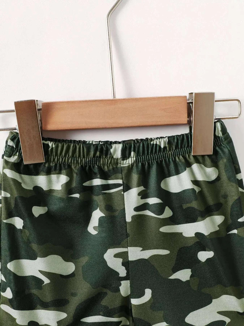 Green camouflage kids' shorts with elastic waistband, held on a hanger