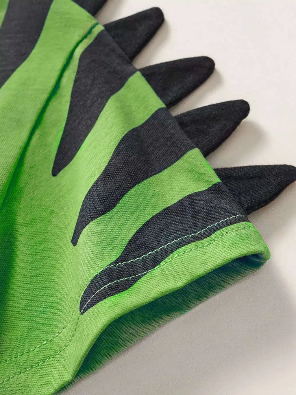 Green dinosaur graphic tee sleeve with black spikes and stitched cuff