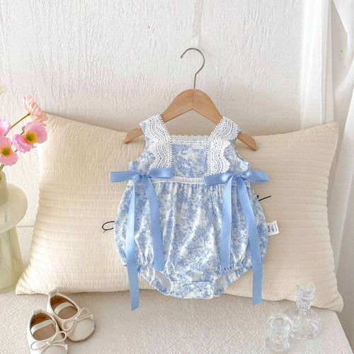 Blue floral baby romper with lace neckline and bow straps, laid on a light cushion