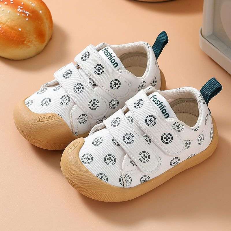 White fabric baby shoes with circular print, two hook-and-loop straps, teal pull tabs