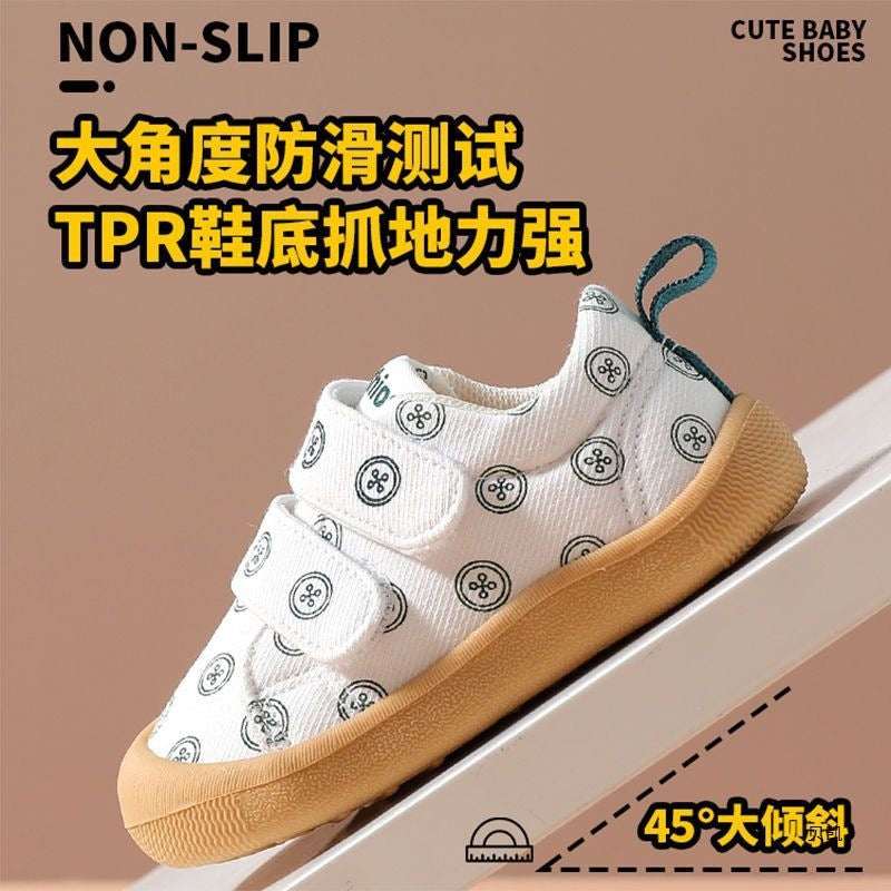 White baby shoes with all-over circular print, teal heel pull, and tan textured sole