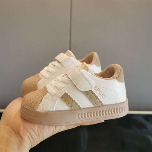 Baby velcro sneakers, white upper with beige sole, side view held in hand.