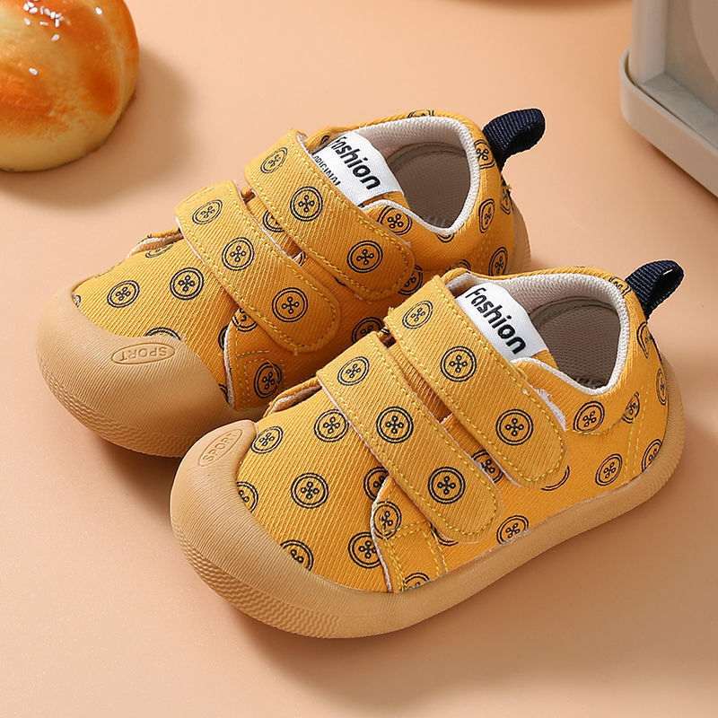 Warm yellow cloth toddler shoes with circular print, teal pull tab, and tan gum sole