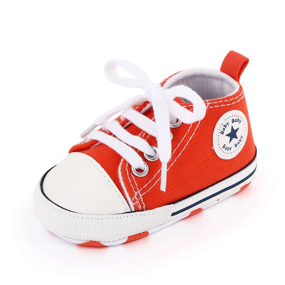 Baby canvas shoes in red-orange with white toe, lace-up front, and star patch
