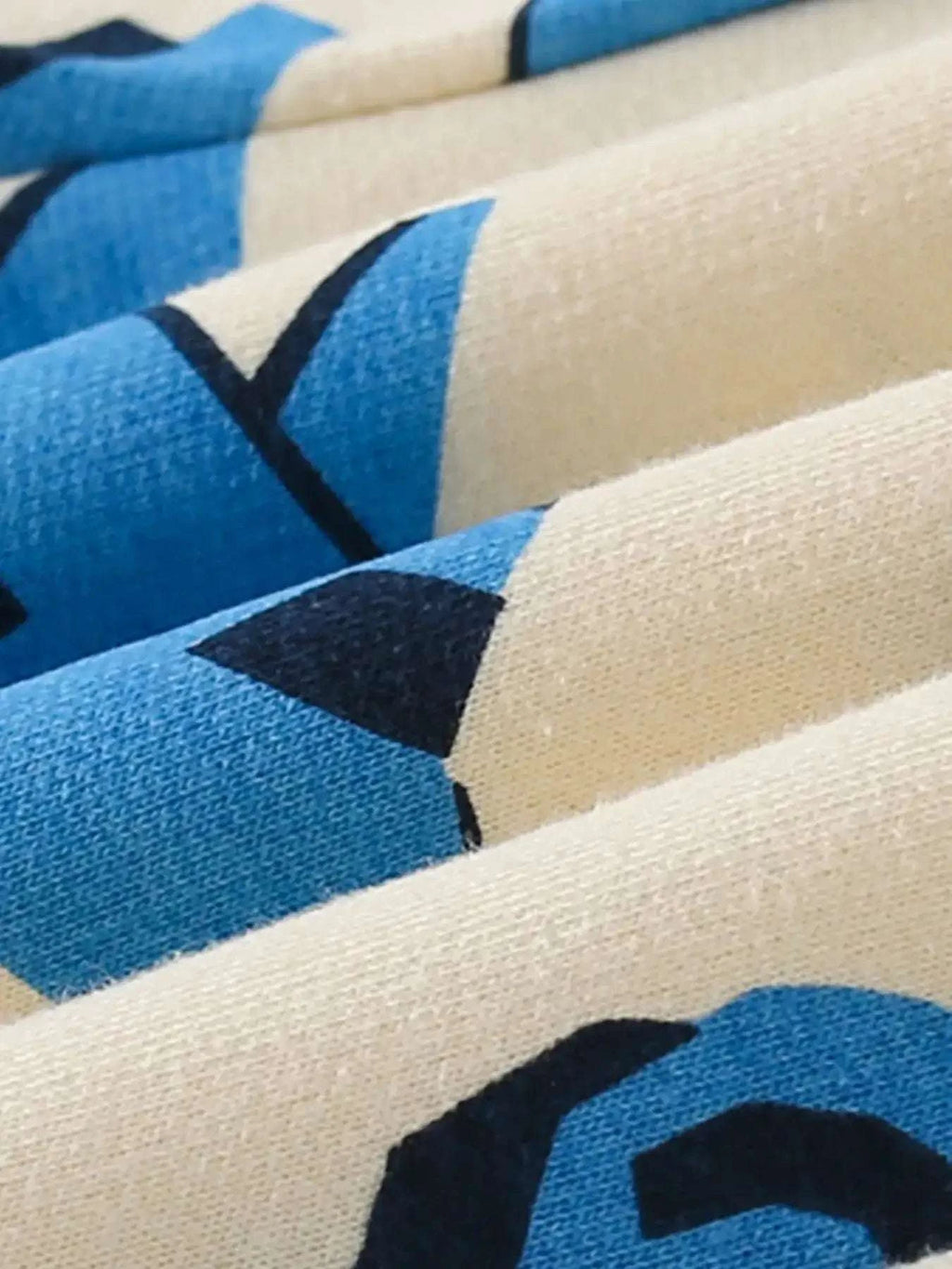 White fabric closeup with blue cartoon dinosaur print and black graphic shapes