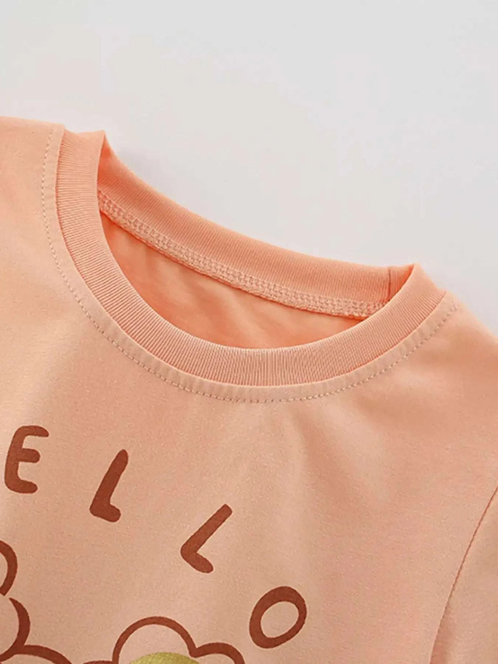 Ruffle-trim children's t-shirt, peach-pink crew neck, partial Hello lettering
