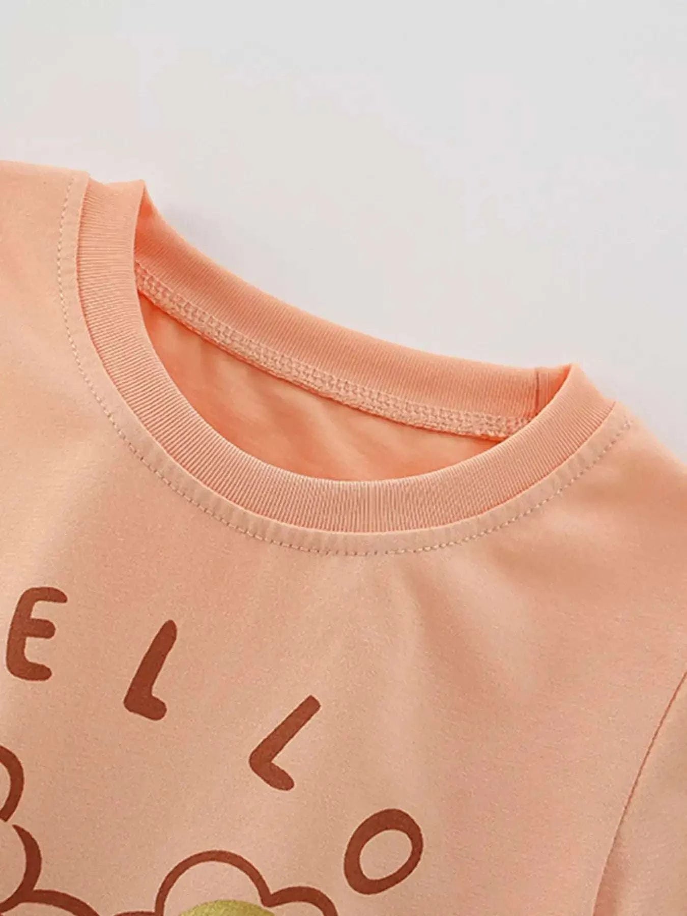 Ruffle-trim children's t-shirt, peach-pink crew neck, partial Hello lettering