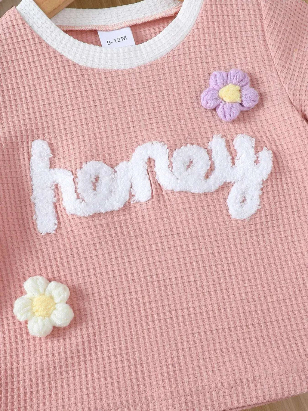 Pink waffle-knit tee with white “honey” lettering and small pastel flower patches